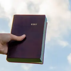 Dłoń trzyma Biblię na tle nieba. Czy to znaczy "Deus Deus Kosmateus"?