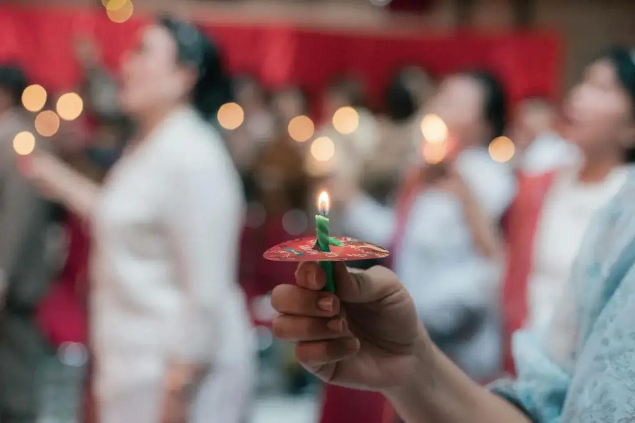Dłoń trzyma zieloną świecę z płomieniem, podczas nabożeństwa. W tle widać ludzi i światła, atmosfera sugeruje post eucharystyczny, grzech ciężki.